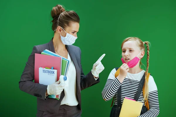 现代女教师 女学生 带着面具和课本 注意佩戴隔离在黑板绿色背景上的面具 — 图库照片