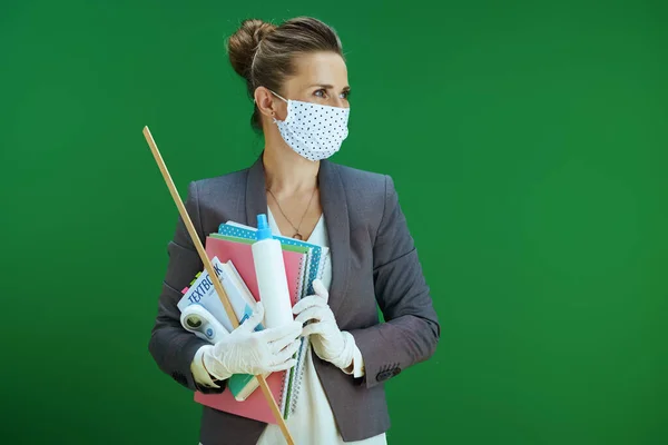Covid 19大流行病期间的生活 现代中年女教师 身穿白衬衫 戴着医疗面罩 橡胶手套 数字温度计 课本和卫生纸 隔离在黑板绿色背景中 — 图库照片
