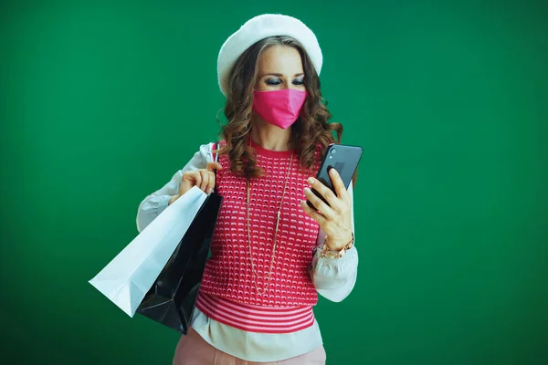 Covid 19大流行病期间的生活 穿着粉色无袖衬衫 戴着粉色医疗面罩 头戴购物袋的优雅女性购物者在互联网上用绿色隔离智能手机购物 — 图库照片