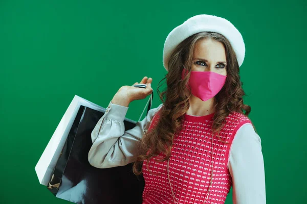 コロナウイルスのパンデミックの間の生活 ピンクの医療マスクとグリーンを背景にしたショッピングバッグを持つ白いベレー帽の流行の女性 — ストック写真