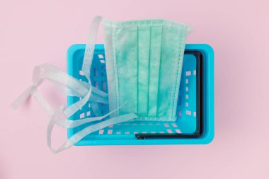 Coronavirus düz yatıyordu. Pembe arka planda tüketici sepeti ve tıbbi maske vardı..