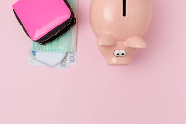 Coronavirus dairesi, domuz kumbarası, cüzdan, avro parası ve pembe arka planda tıbbi maskeyle yatıyordu..