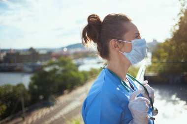 Koronavirüs salgını. Steteskoplu ve tıbbi maskeli modern tıp doktoru şehrin dışındaki mesafeye bakıyor..