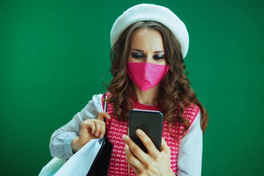 Koronavirüs salgını sırasında hayat. Pembe kolsuz gömlekli, şık bir kadın. Pembe tıbbi maskeli ve alışveriş çantalı. Çevrimiçi alışveriş yapıyor..