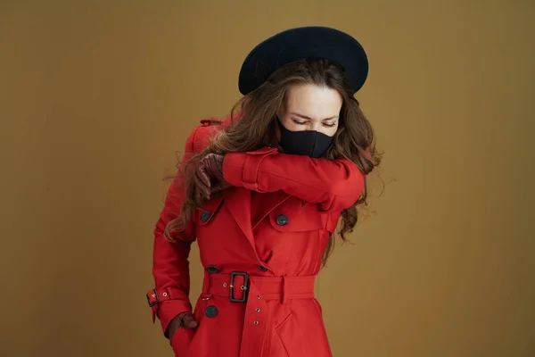 コロナウイルスのパンデミックの間の生活 トレンディーな中年女性で赤コートに黒マスクスニーズに肘に茶色の背景 — ストック写真