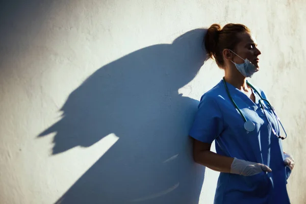コロナウイルスのパンデミック 壁の近くの街で聴診器 医療用マスク ゴム手袋と一致して疲れ現代医師の女性 — ストック写真