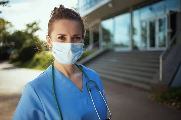 Covid 19大流行病 诊所外穿着制服 戴听诊器 戴口罩的现代女医生的画像 — 图库照片