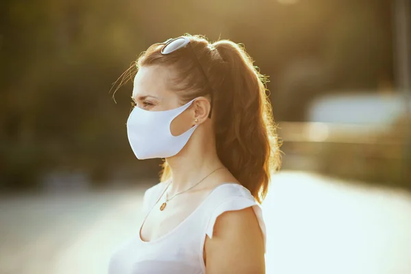 pensive modern woman in pink blouse with white mask and sunglasses looking into the distance outdoors in the city.