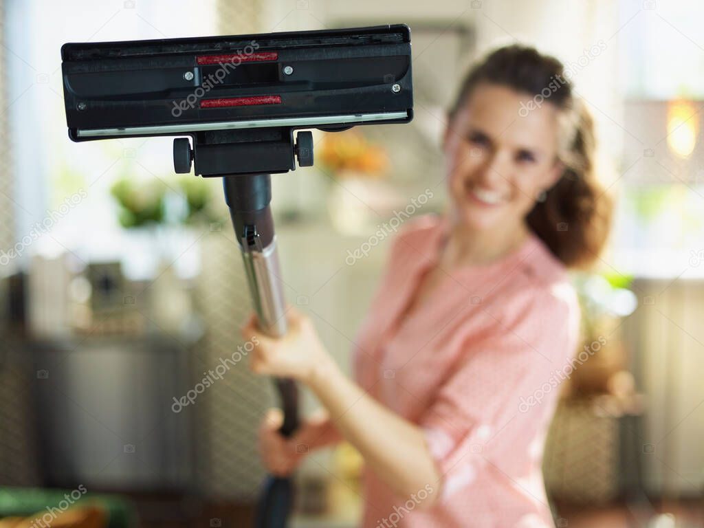 Closeup on happy woman in blouse and white pants with vacuum cleaner brush at home in sunny day.