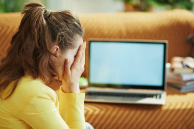 Güneşli bir günde modern evde, dizüstü bilgisayar boş ekranının yanında sarı ceketli 40 yaşında zarif bir kadın vardı..