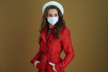 Koronavirüs salgını sırasında hayat. Kırmızı ceketli düşünceli bir kadın bej arka plandaki mesafeye bakıyor..