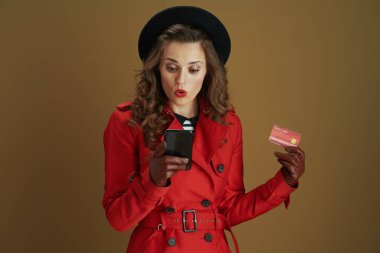 Merhaba Ekim. 40 yaşında, kırmızı ceketli, siyah bereli, akıllı telefon, kredi kartı ve bej arka planda izole deri eldivenli zarif bir kadın..