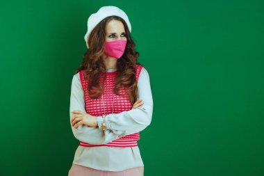 Covid-19 salgını sırasında hayat. Pembe kolsuz gömlekli, yeşil arka planda pembe tıbbi maskeli zarif bir kadın..