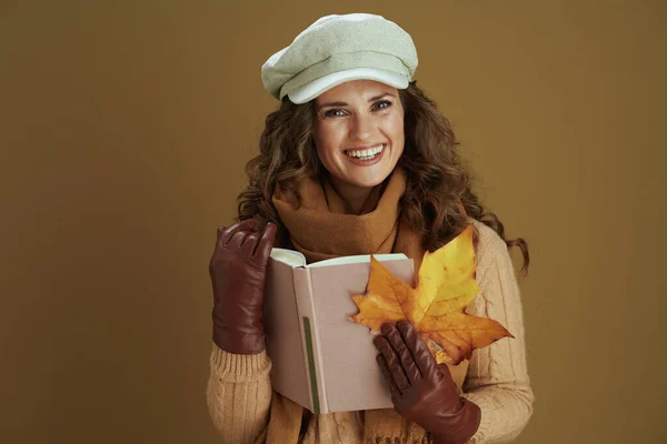 幸せな中年齢の女性でセーターとともに黄色の秋のカエデの葉 本と革手袋で茶色の背景 — ストック写真