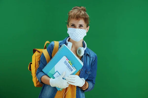 在大肠病毒大流行期间的生命 身穿黄色衬衫 头戴课本 笔记本 医疗面罩 白色耳机和绿色背景背包的年轻女学习者 — 图库照片