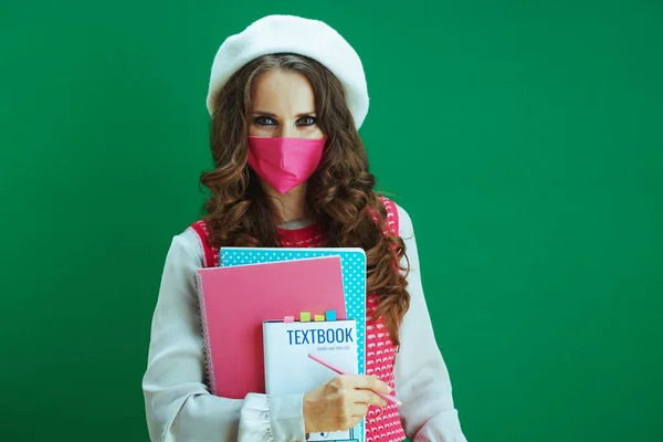 Covid 19大流行病期间的生活 身穿白色贝雷帽的年轻女性形象 带着课本 笔记本和粉色医疗面罩 与绿色隔离 — 图库照片