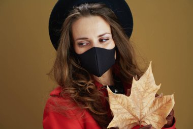 Koronavirüs salgını sırasında hayat. Siyah maskeli orta yaşlı ev kadını ve bronz arka planda sarı sonbahar akçaağaç yaprağı..