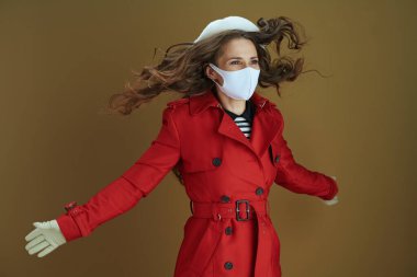 Covid-19 salgını sırasında hayat. Kahverengi arka plana atlayan kırmızı ceketli neşeli, orta yaşlı bir kadın..