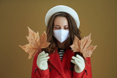 Merhaba sonbahar. Sarı sonbahar akçaağaç yaprağıyla bej arka planda izole edilmiş kırmızı ceketli şık bir kadın..