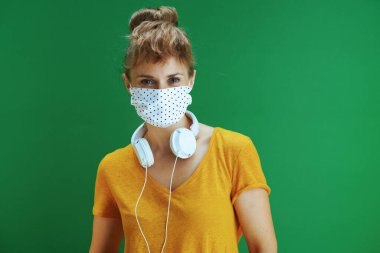 Covid-19 salgını sırasında hayat. Sarı gömlekli, tıbbi maskeli ve yeşil arka planda beyaz kulaklıklı genç bir kızın portresi..