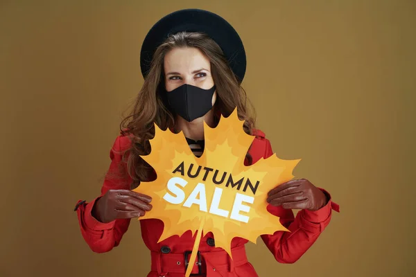 Covid 19大流行病期间的生活 40岁的女人 身穿红色外套 挂着秋天销售的叶状横幅和褐色背景的黑色面具 面带微笑 — 图库照片