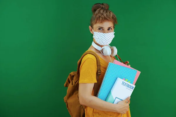 在大肠病毒大流行期间的生命 穿着黄色衬衫的学生 带着课本 笔记本 医疗面罩 白色耳机和背包 在绿色背景下看复印空间 — 图库照片