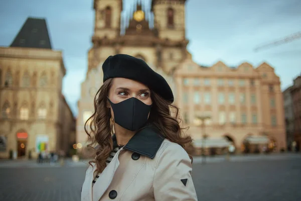 現代的な中年女性でベージュトレンチコートと黒ベレー帽で黒マスクで旧市街広場プラハ — ストック写真