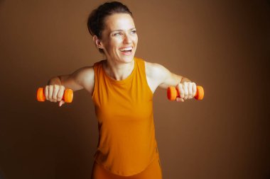 Aktif kıyafetli gülümseyen bir kadın, neşeli ve sağlıklı bir formda, gücünü ve kararlılığını göstermek için dambıllarıyla göğüs sineği gösterisi yapıyor..