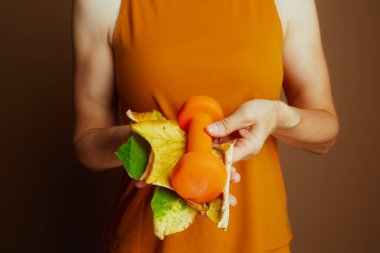 Yakın çekim, sonbahar yapraklarının arasına yerleştirilmiş turuncu bir dambıl yakalıyor. Sonbahar sezonunda sporu ve dayanıklılık eğitimini simgeliyor..