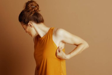 Profil görüntüsüne göre, hardal sarısı atletli bir kadın koltukaltına doğru nazikçe kumaş sıkıyor ve aşağıya bakıyor. Bu, özel bir kişisel muayene ya da sağlık sorununu gösteriyor.