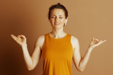 Çörekli, hardal sarısı bluzlu orta yaşlı bir kadın, gözleri kapalı, elleri kulaklık takmış, iç huzuruyla gülümsüyor..