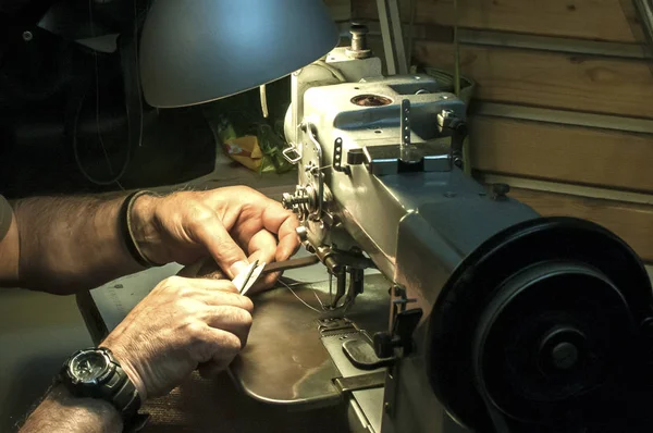 Leather tailor man hands making leather bag of sewing machine closeup as scene of working process