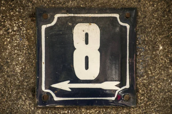 Weathered grunge square metal enameled plate of number of street address with number 8 closeup