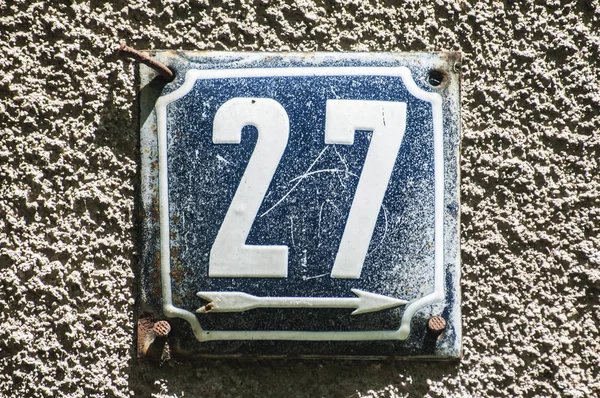 Weathered grunge square metal enameled plate of number of street address with number 27 closeup