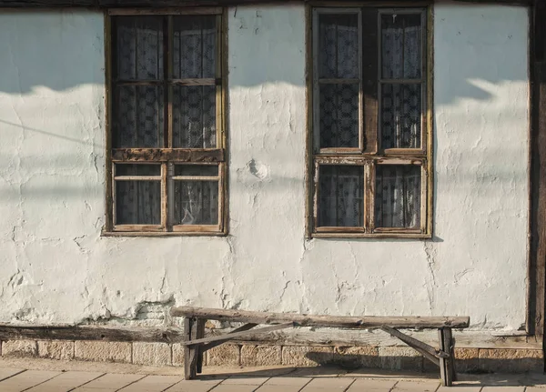 Old country house facade with weathered wooden windows and bench in sunny day