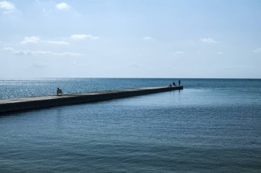 Berrak güneşli yaz gününde sakin mavi deniz suları ve üç insan siluetleri deniz koyunda Taş rıhtım