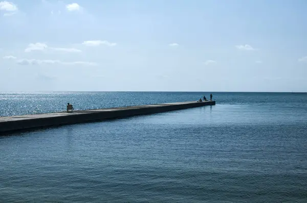 Berrak güneşli yaz gününde sakin mavi deniz suları ve üç insan siluetleri deniz koyunda Taş rıhtım