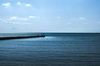 Berrak güneşli yaz gününde sakin mavi deniz suları ve üç insan siluetleri deniz koyunda Taş rıhtım