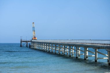 Berrak yaz gününde mavi gökyüzü arka plan üzerinde sakin deniz suları arasında endüstriyel vinç ile iskeleye görünümü