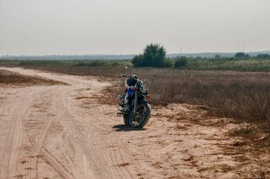 Motorsiklet güneşli yaz gününde terk edilmiş kumlu yolda durdu.