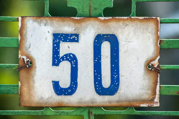 Weathered grunge square metal enameled plate of number of street address with number 50 closeup
