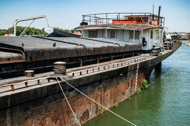 Ağır paslanmış eski bir nehir mavnası. İhmal edilmiş bir sanayi limanındaki giriş platformuna demirlemiş.