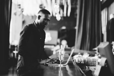 Yakışıklı Afrikalı genç bir adam dizüstü bilgisayar ekranına bakıyor. Zenci işadamı kulüpte dizüstü bilgisayarla çalışıyor..