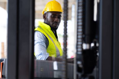 Depoda çalışan işçi sürücü forklift. Depoda forkliftle kart kutuları istifleyen bir depo çalışanı. Afrikalı Amerikalı siyahiler.