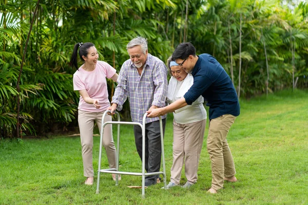 A family is trying to help Dad to walk because father is paralysed on lawn at home. paralysis and walking crutch concept.