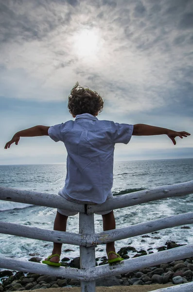 Criança relaxante na praia, abrindo os braços contra o fundo do mar e do céu — Fotografia de Stock