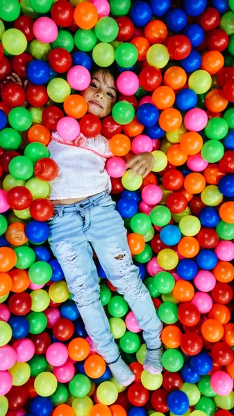 Pequena menina sorrindo jogando deitado em bolas coloridas — Fotografia de Stock