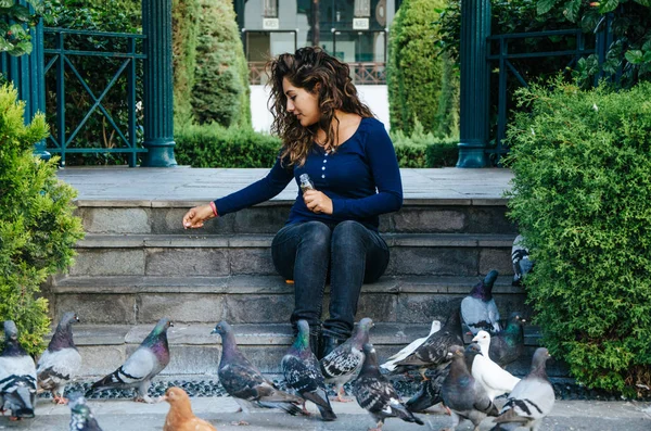 Красива усміхнена жінка годує голубів в парку протягом дня — стокове фото