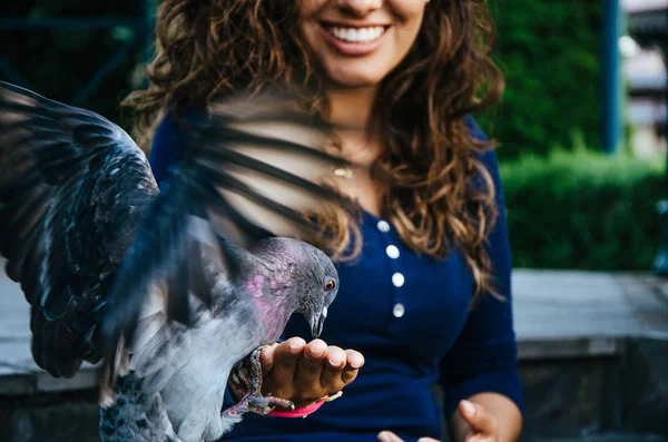 Bir güvercin elini besleyen bir gülümseyen kadın — Stok fotoğraf
