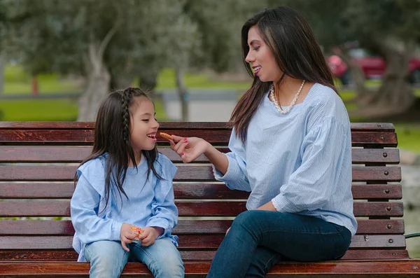 Mère et sa petite fille assises sur un banc mangeant un cookie — Photo